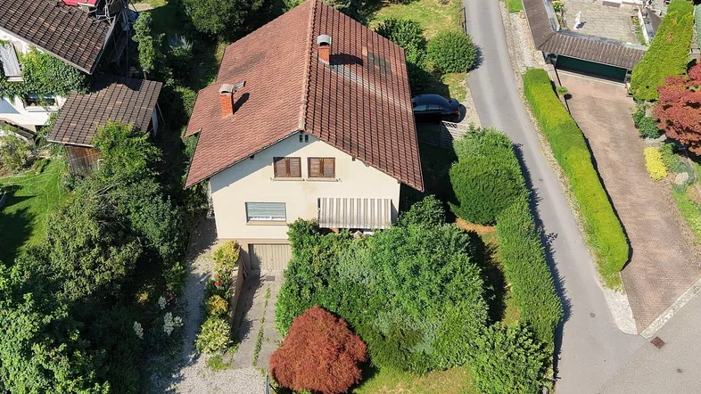 Luftaufnahme eines Einfamilienhauses mit Garten, Zufahrt und kleinem Balkon in einer Wohngegend.