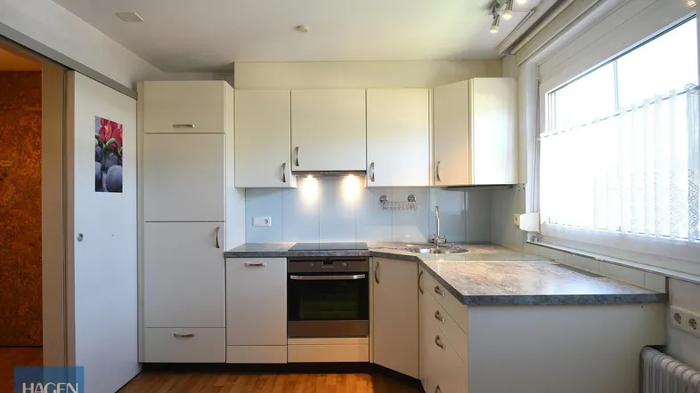 Helle Einbauküche mit weißen Schränken, integriertem Backofen und Holzfußboden.