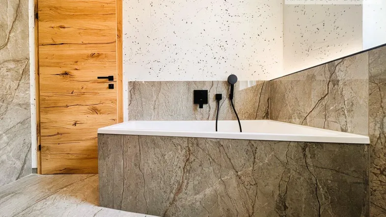 Modernes Badezimmer mit integrierter Badewanne, großformatigen Fliesen und Holztür.