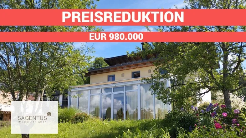 Hausfassade mit Wintergarten und grüner Umgebung unter blauem Himmel, mit Preisreduktionsbanner.