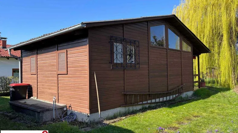 Charmantes Holzhaus mit Garten und sonniger Lage unter einem Weidenbaum.