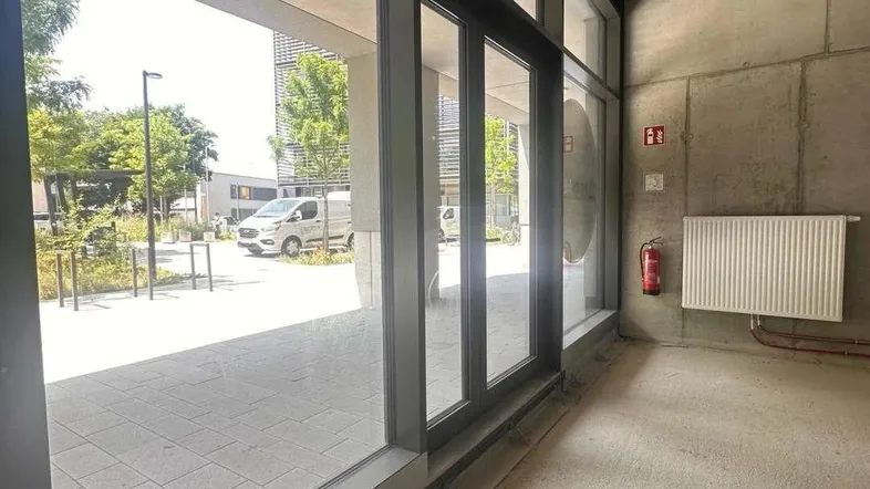 Unfertiger Innenraum eines Gewerbeobjekts mit großen Fenstern und Blick auf den Außenbereich.