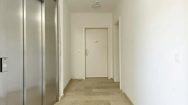 Heller Eingangsbereich mit Fliesenboden und modernem Aufzug, der zu den Wohneinheiten führt.