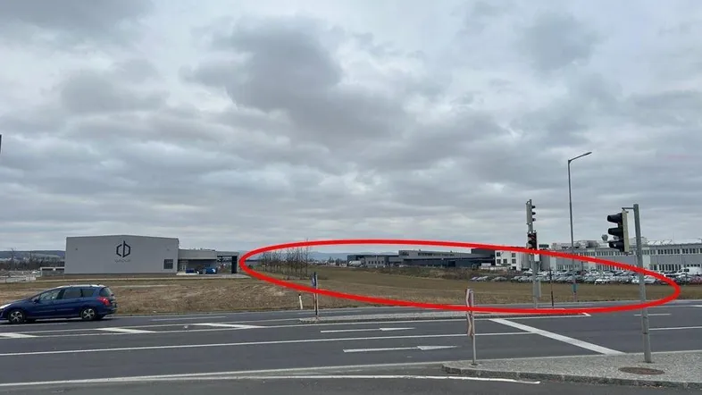 Blick auf ein Industriegebiet mit Straße, Gebäuden und freiem Feld unter bewölktem Himmel.