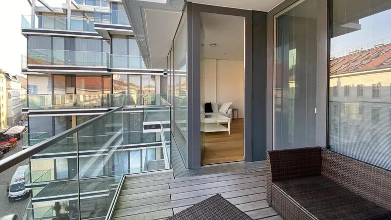 Balkon mit Rattanmöbeln und Blick auf die moderne Gebäudefassade und den Innenbereich.