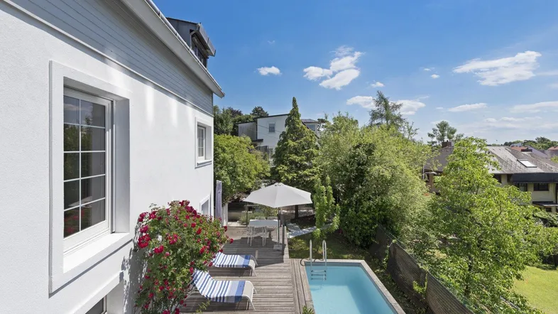 Große Holzterrasse mit kleinem Pool, Sonnenliegen und Blick ins Grüne.