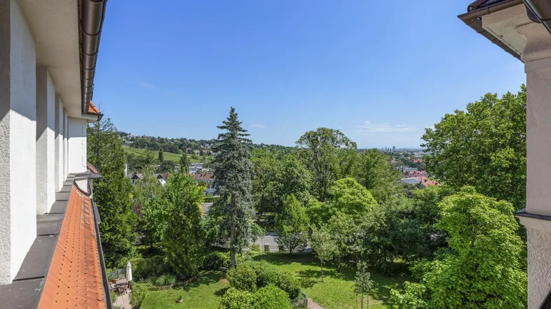 Weitläufiger Blick von einem Balkon über eine grüne Landschaft bis zur entfernten Stadtkulisse.