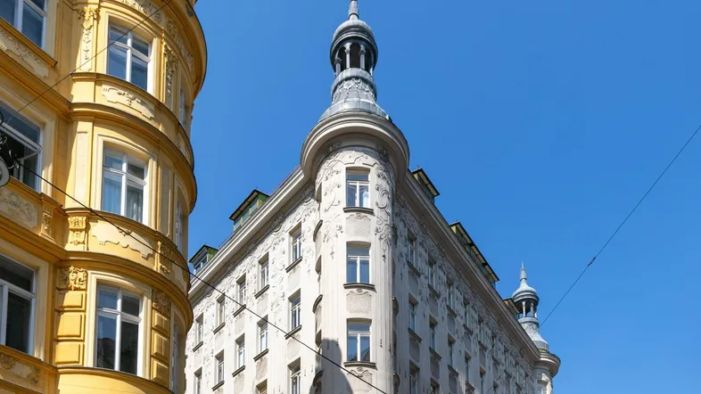 Historische Gebäude mit kunstvollen Fassaden und einem markanten Eckturm unter blauem Himmel.