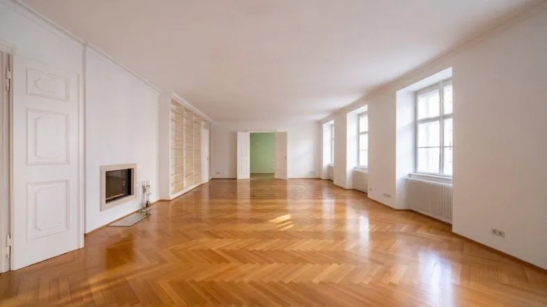 Geräumiges Wohnzimmer mit Fischgrätparkett, Kamin und hohen Fenstern, das viel Tageslicht bietet.