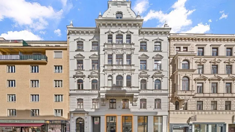 Historisches Gebäude mit aufwendiger Fassade und Geschäftsflächen im Erdgeschoss an einer belebten Straße.