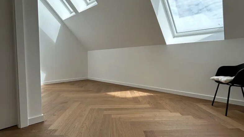 Helles Dachgeschosszimmer mit schrägem Dach und zwei Dachfenstern, ausgestattet mit Fischgrätparkett.