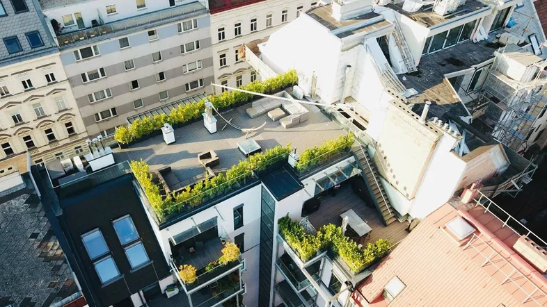 Luftaufnahme von modernen Dachterrassen mit Begrünung und umliegenden Gebäuden in der Stadt.