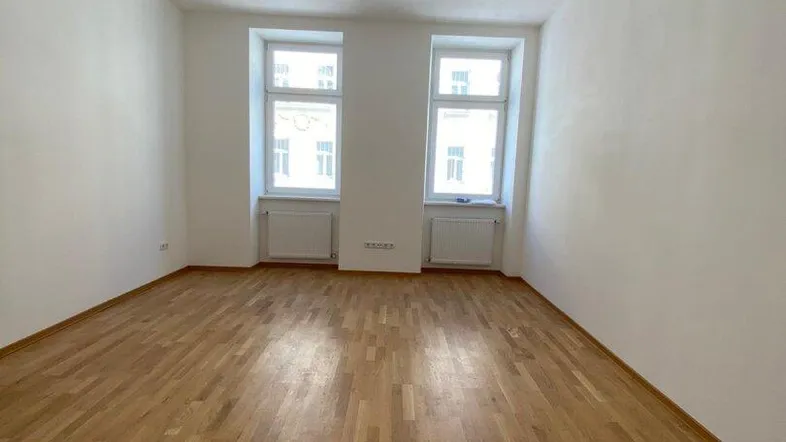 Heller, leerer Raum mit Parkettboden und zwei Fenstern, bereit zur individuellen Gestaltung.