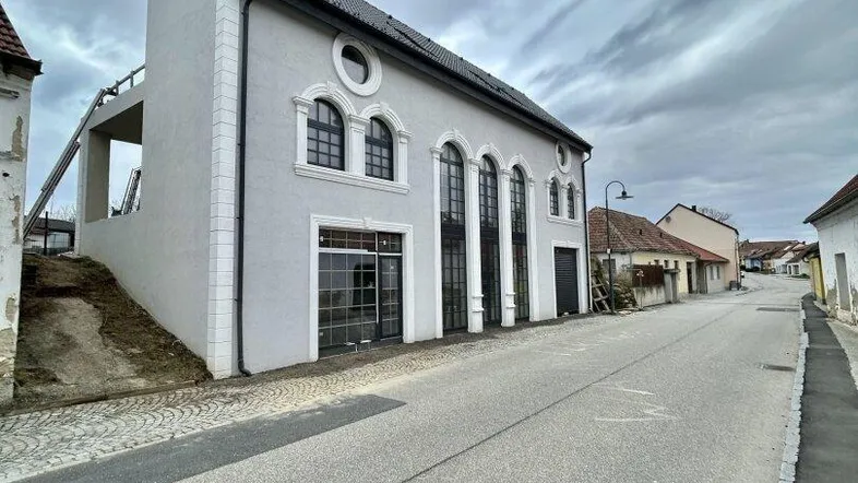 Modernes Gebäude mit großen Bogenfenstern und einer schrägen Dachlinie an einer ruhigen Straße.