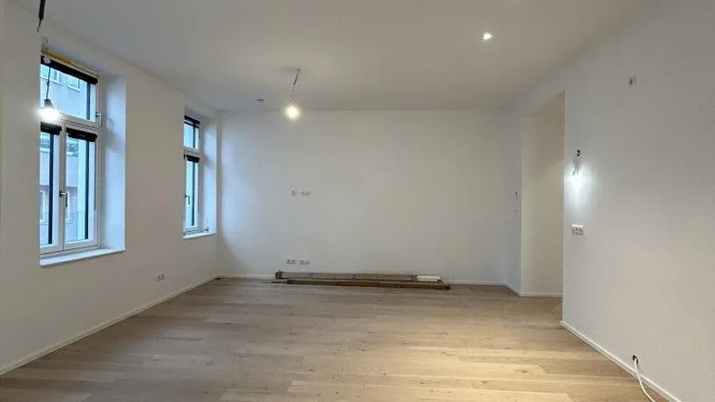 Heller, leerer Raum mit neuem Holzparkettboden und Einbaustrahlern an der Decke.