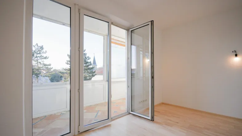 Helles Wohnzimmer mit Parkettboden und Zugang zu einem gefliesten Balkon mit Blick ins Grüne.