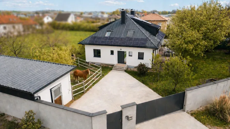 Luftaufnahme eines modernen Einfamilienhauses mit Solaranlage, großem Grundstück und Pferd auf der Weide.