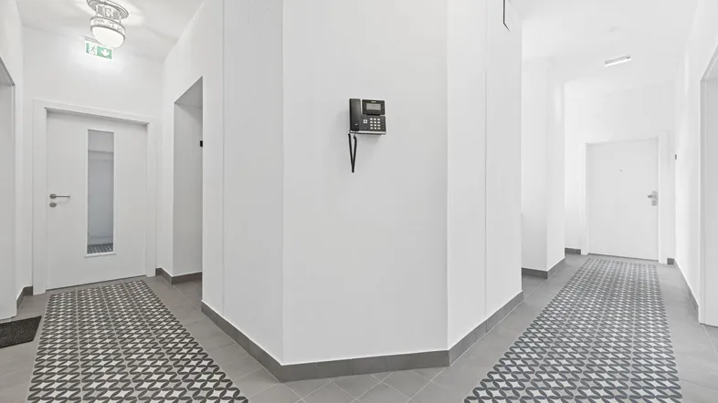 Heller Flur mit modernen Fliesen und Gegensprechanlage, der zu verschiedenen Wohnungen führt.