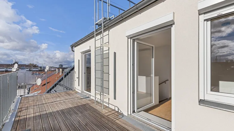 Geräumige Holzterrasse mit Metallgeländer und Zugang zum Gebäude, umgeben von Stadtdächern.