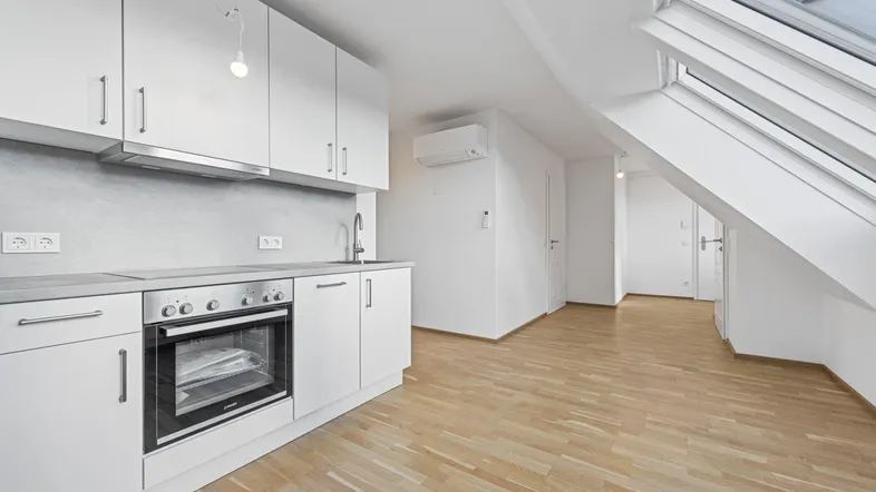 Helle Küchenzeile in einer Dachgeschosswohnung mit Holzboden und Dachfenstern.