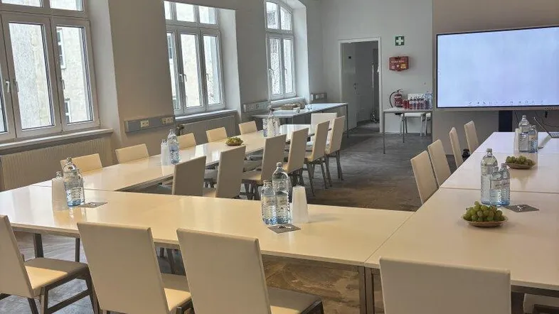 Großer Konferenzraum mit modernen Tischen, Stühlen und einem großen Bildschirm, ideal für Besprechungen.