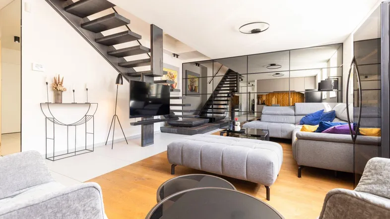 Modernes Wohnzimmer mit offener Treppe, Holzboden und stilvollen Möbeln, durch Spiegelwand erweitert.