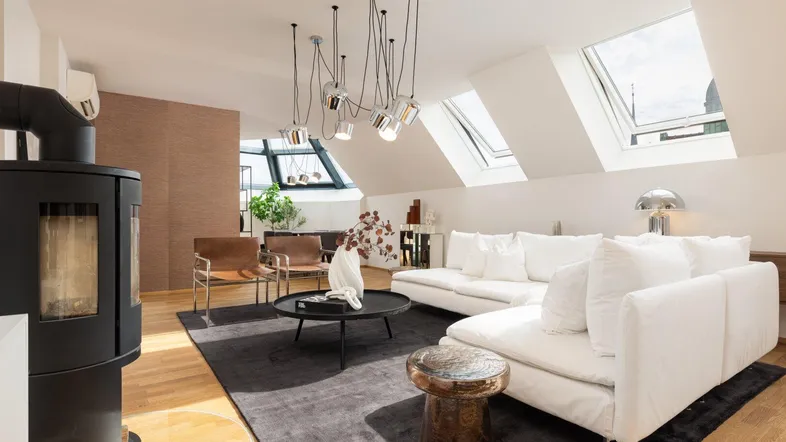 Helles und modernes Wohnzimmer im Dachgeschoss mit Kaminofen, Holzboden und großen Dachfenstern.