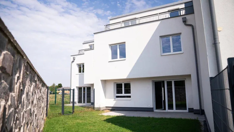 Moderne weiße Reihenhäuser mit kleinen privaten Gärten und einer Steinmauer im Vordergrund.