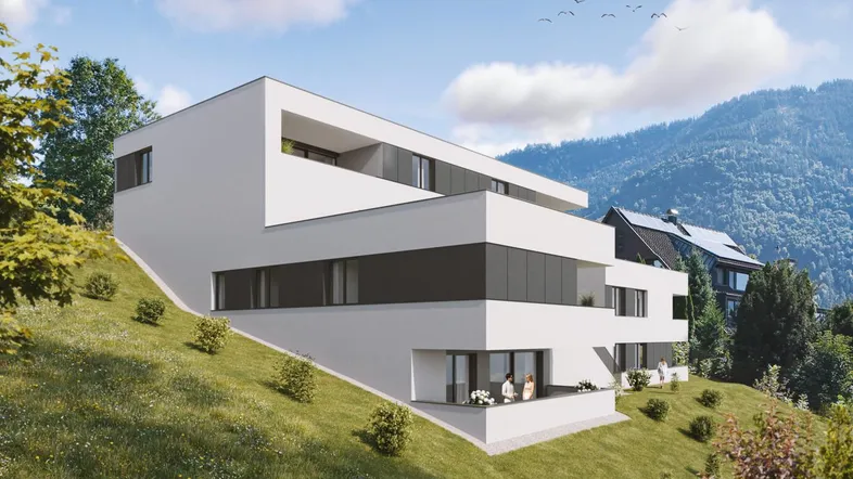 Modernes, weisses Mehrfamilienhaus mit grossen Fenstern und Balkonen am Hang in Feldkirch, umgeben von grünen Wiesen und Bergen (Rauhenweg).