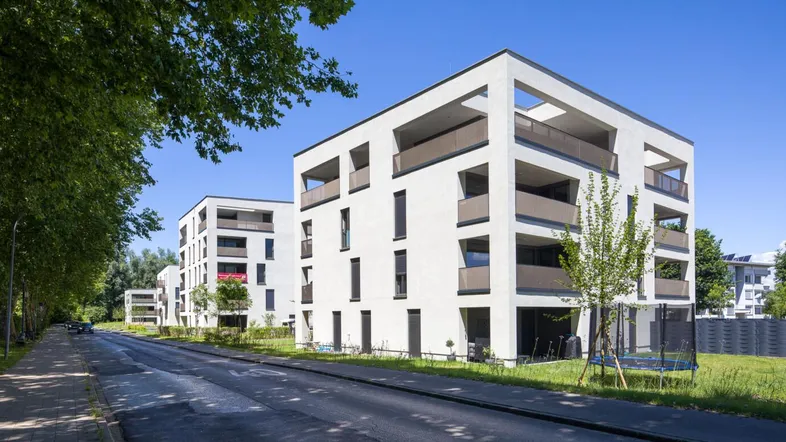 Moderne Mehrfamilienhäuser mit klaren Linien und Balkonen entlang einer grünen Straße.