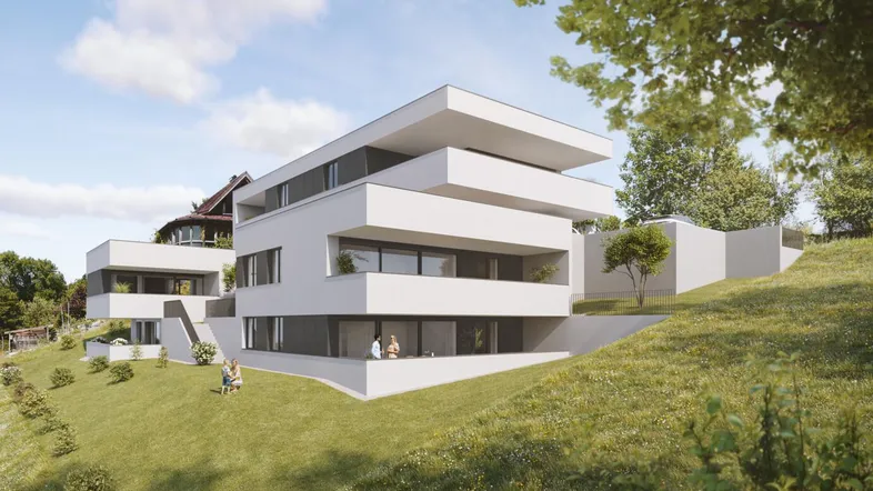 Zwei moderne weiße Wohngebäude mit Terrassen und Balkonen am Hang in Feldkirch-Rauhenweg, grüner Rasen und Bäume umgeben.