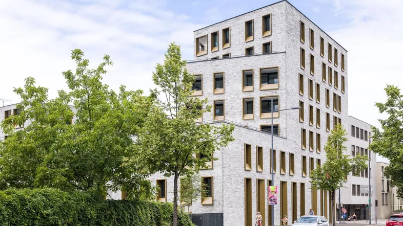 Modernes Mehrfamilienhaus mit heller Fassade und markanten Fenstern an einer belebten Straße.