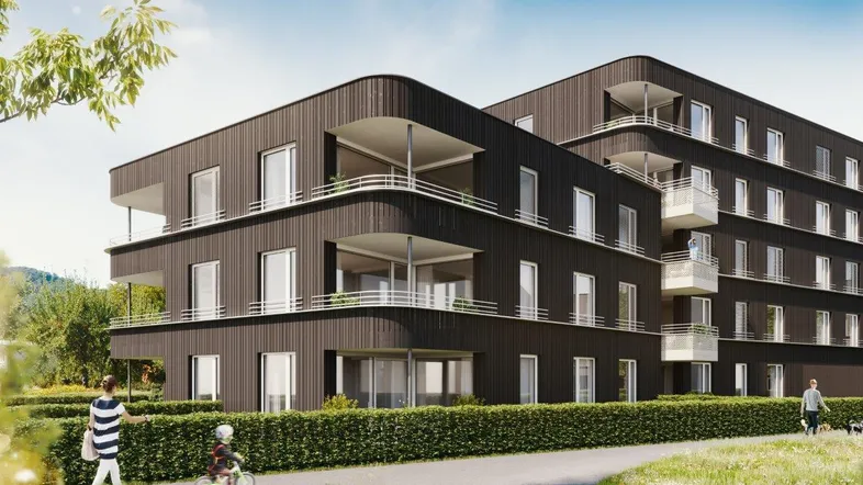 Modernes Mehrfamilienhaus mit dunkler Fassade, geschwungenen Balkonen und grüner Umgebung.