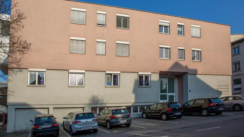 Aussenansicht des Gebäudes Brielgasse 27 in Bregenz mit Parkplätzen davor und blauer Himmel