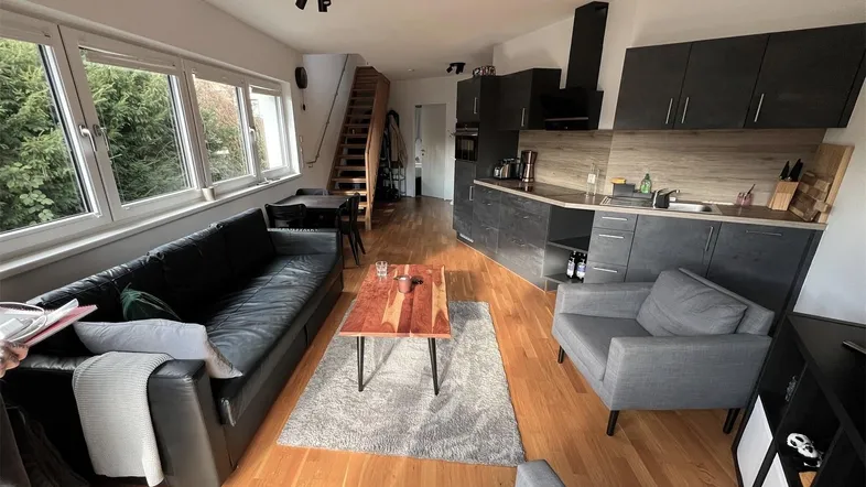 Offener Wohn- und Küchenbereich mit Holzboden, moderner Einbauküche und gemütlicher Sitzecke.