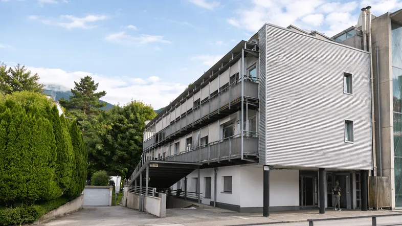Modernes Mehrfamilienhaus mit Balkonen und Metallfassade in grüner Umgebung.
