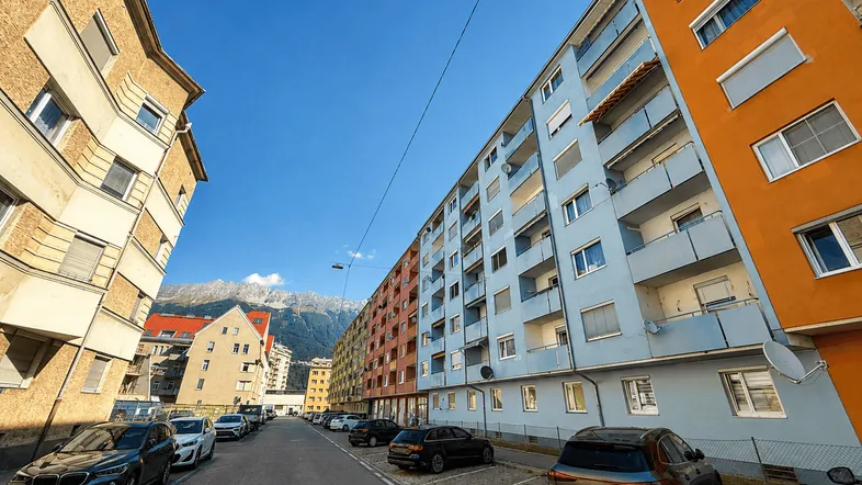 Wohngebäude in einer städtischen Umgebung mit geparkten Autos und Bergblick im Hintergrund.