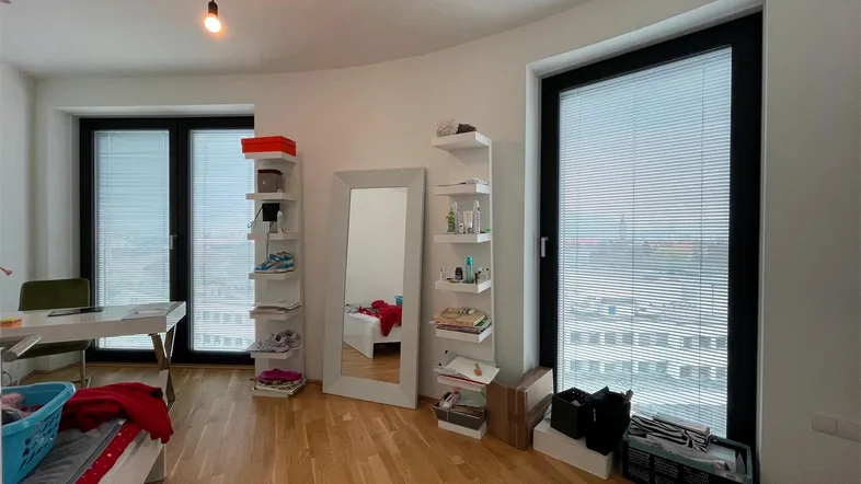 Helles Schlafzimmer mit Parkettboden, großen Fenstern, Stadtblick und moderner Einrichtung.