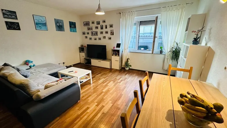 Heller Wohn- und Essbereich mit Parkettboden, gemütlichem Sofa und Esstisch am Fenster.