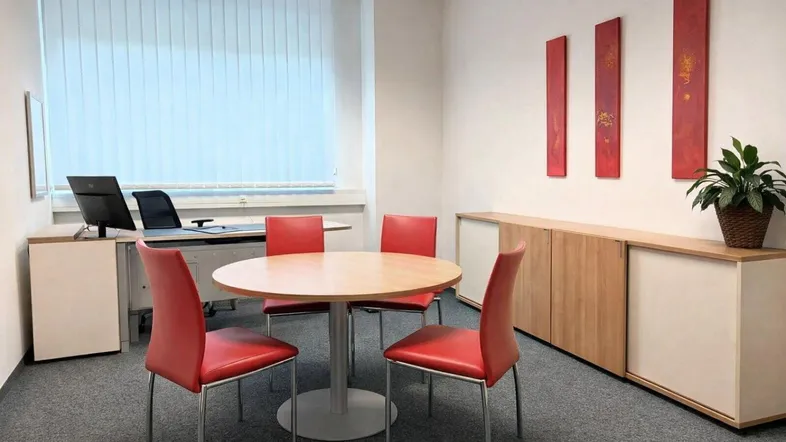 Heller Büroraum mit modernem runden Tisch, roten Stühlen und praktischen Schränken für Besprechungen.