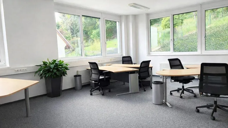 Helles Büro mit mehreren Arbeitsplätzen, großen Fenstern und einem angenehmen Blick ins Grüne.