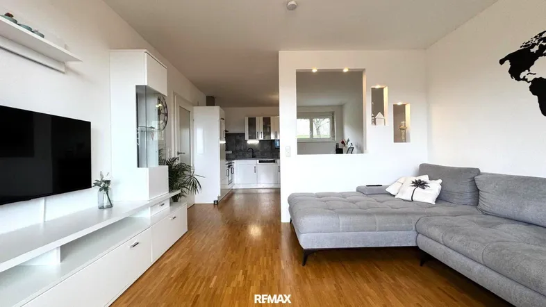 Helles Wohnzimmer mit modernem Sofa, weißem TV-Möbel und offenem Übergang zur Küche.