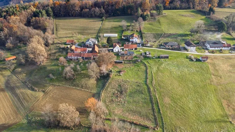 Luftaufnahme einer ländlichen Siedlung mit Feldern und Wäldern im Herbst, umgeben von sanften Hügeln.