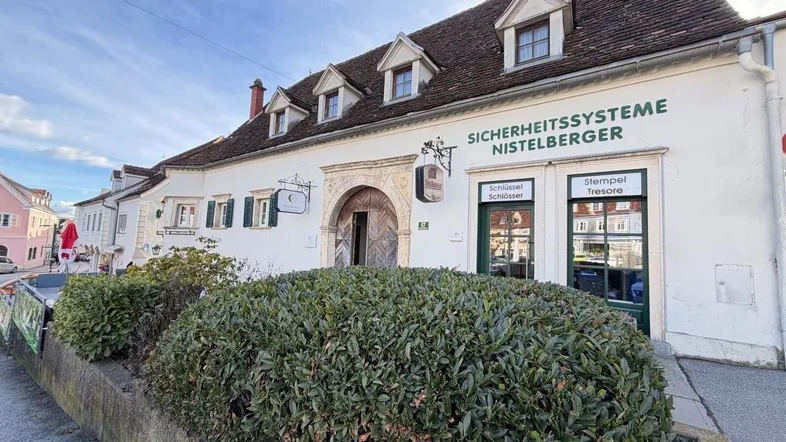 Historisches Gebäude mit weißer Fassade, Dachgauben und Geschäftsfront in einer belebten Straße.