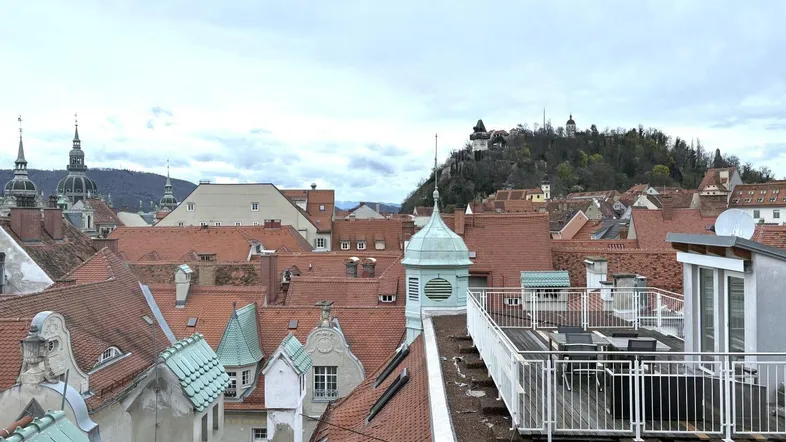 Dachterrasse mit Panoramablick über die Stadt, rote Ziegeldächer und eine Burg auf dem Hügel im Hintergrund.