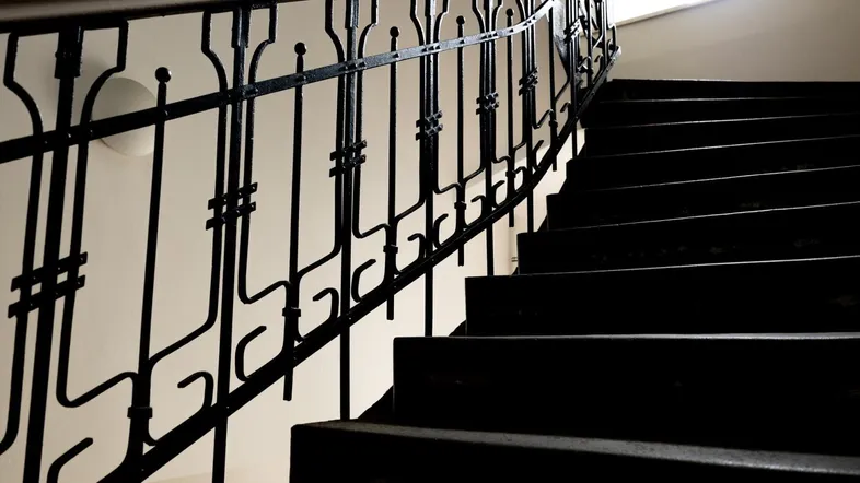 Elegantes Treppenhaus mit schmiedeeisernem Geländer und dunklen Stufen in einem Altbau.