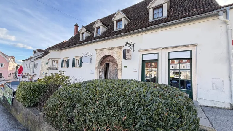 Historisches Gebäude mit weißer Fassade, traditionellem Dach und gepflegter Hecke im Vordergrund.