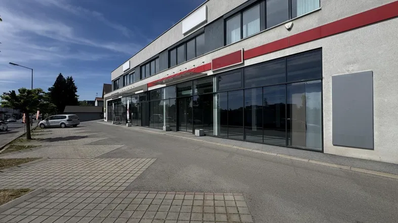 Außenansicht eines modernen Geschäftsgebäudes mit großen Glasfronten und Parkplätzen davor unter blauem Himmel.