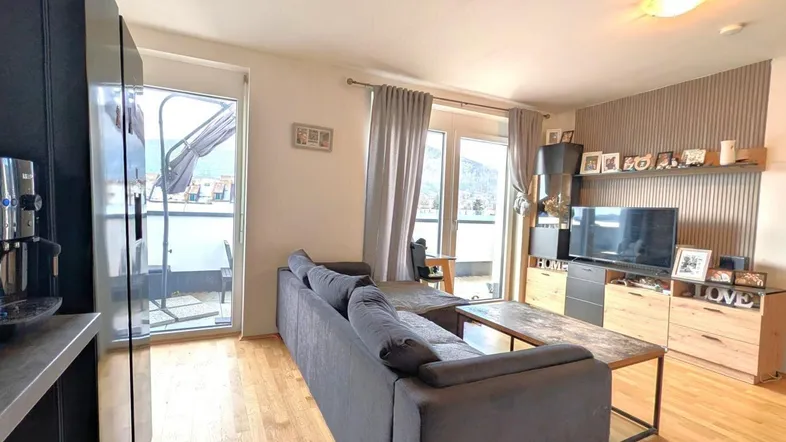 Helles Wohnzimmer mit Holzboden, gemütlichem Sofa und Zugang zu einem Balkon.