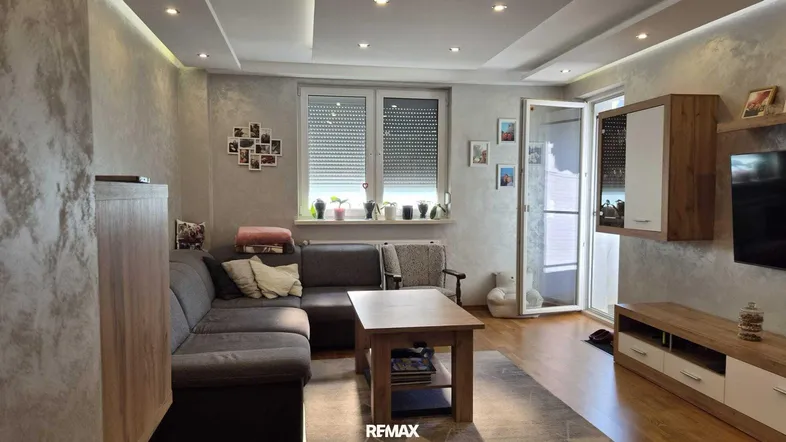 Gemütliches Wohnzimmer mit bequemer Couch, Holztisch und Zugang zu einem sonnigen Balkon.